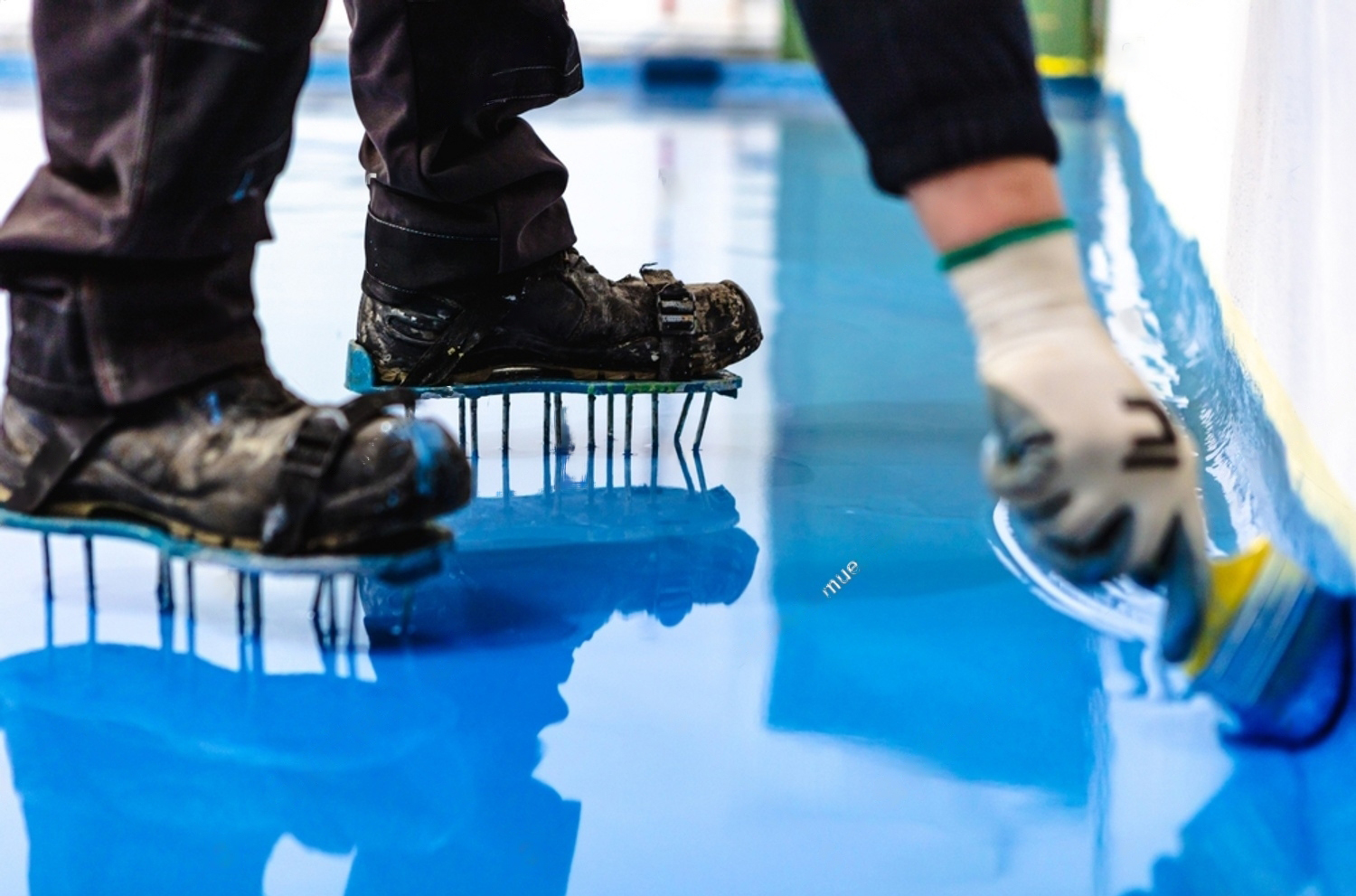 Applicator in spiked shoes back-rolling a fresh blue epoxy floor